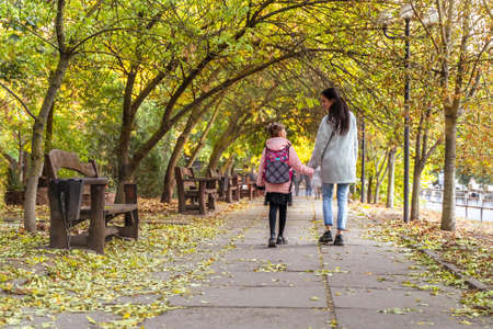 Happy mom and daughter walk in autumn park. Little girl after school with mother. Everyday lifeの写真素材