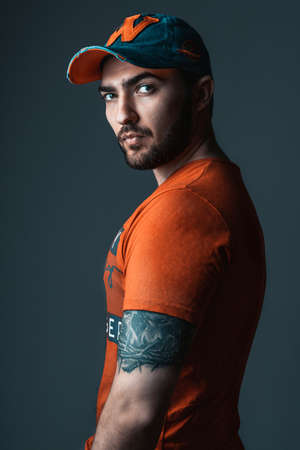 POLAND, BYDGOSZCZ - May 16, 2021: Handsome man with beard on dark background. Stylish guy in cap and t-shirt in studio.の写真素材