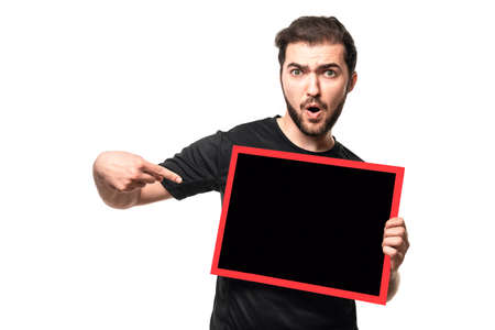 Guy with open mouth points finger space for your text or ad on poster. Surprised man in black t-shirt shows advertisement in studioの写真素材