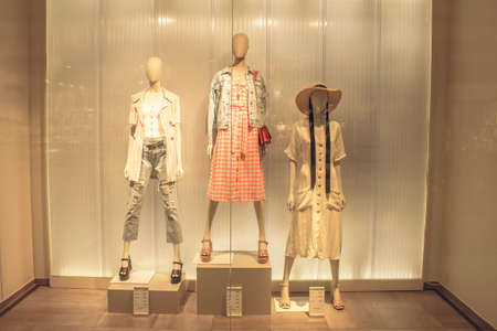 Portrait of human female blonde mannequin in shop window. Dummy head on orange warm autumn background. White doll with red lips and white earrings in jacketの写真素材