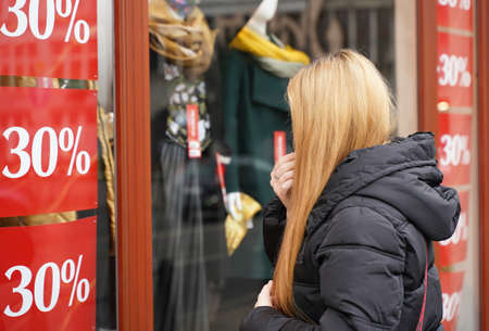 Curious woman looks clearance shop window at mannequins. Girl customer near store. Black Friday discounts sale. Female shoppingの写真素材
