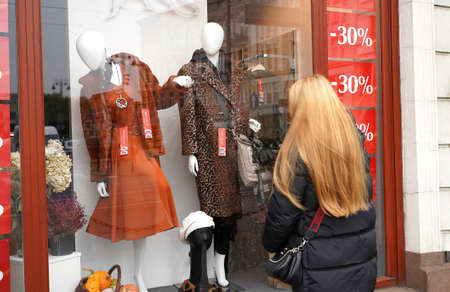 Curious woman looks clearance shop window at mannequins. Girl customer near store. Black Friday discounts sale. Female shoppingの写真素材