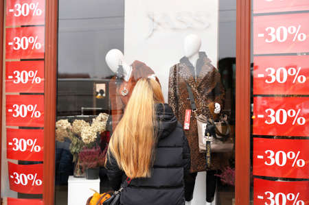 Curious woman looks clearance shop window at mannequins. Girl customer near store. Black Friday...