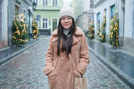 Asian woman enjoy coffee and snowfall outdoors. Cute girl in snowy winter weather