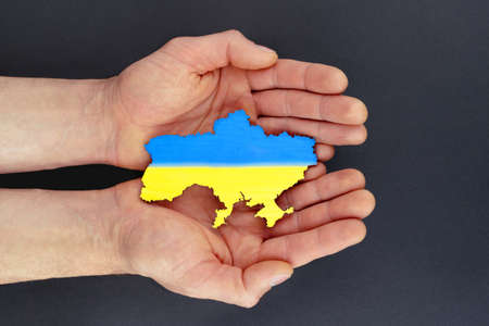 Male hands hold map of Ukraine on black background. Ukrainian blue yellow flag. conceptの写真素材
