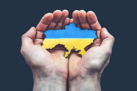 Male hands hold map of Ukraine on black background. Ukrainian blue yellow flag. conceptの写真素材