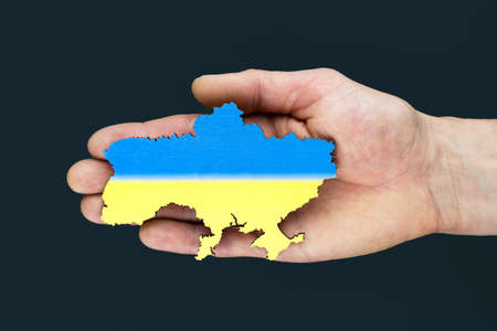Male hands hold map of Ukraine on black background. Ukrainian blue yellow flag. conceptの写真素材