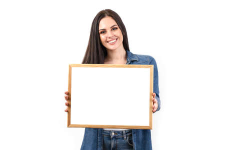 Happy smiling woman holding a poster on a white background in the studio. A beautiful girl shows an advertisementの写真素材