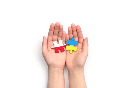 Hands hold two puzzles with flags of Poland and Ukraine on white background. unity solidarity partnership help conceptの写真素材
