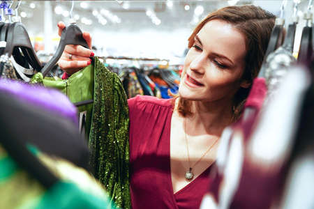 Pretty woman trying on clothes in dressing room in store. Happy buyer girl choose dress. Shoppingの写真素材