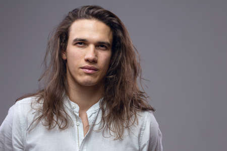 Handsome calm man. Portrait of a young muscular guy with long hair. Strong boy on an isolated gray background in the studioの写真素材