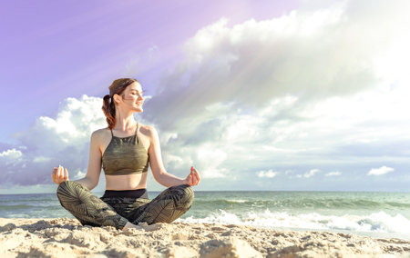 Woman in lotus position on the beach. Girl enjoys meditation outdoors. Yoga harmony of soul and body healingの写真素材