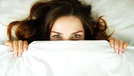 Woman in bed covered her face with blanket. Concept of insomnia or fear. Place for your text or adの写真素材