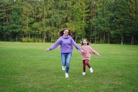 Happy mom and daughter run outdoors. Joyful girl and woman have fun together. Family vacation in natureの写真素材