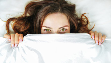 Woman in bed. Girl hides her face under the covers.Concept of healthy sleep, insomnia, comfort zoneの写真素材