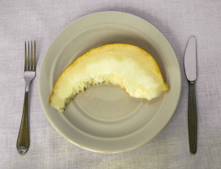 Top view of a piece of melon on a plate with a knife and fork