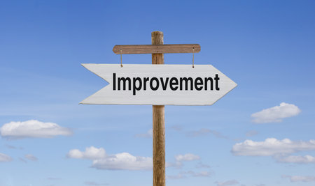 Against the sky, on a wooden stand, a white wooden arrow is suspended by ropes with the inscription: Improvementの写真素材