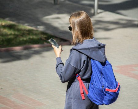 A girl with a mobile phone and a backpack is walking down the street.の写真素材