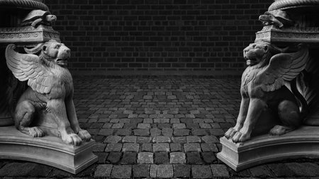 Two sculptures of winged lions stand on paving stones against a brick wall.の写真素材