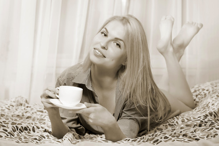 Woman lying at the bed and drinking coffee and smiling. Sepia toned.の写真素材