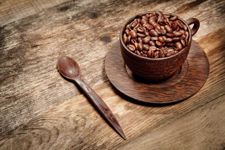 Wooden cup with coffee-beans on old wooden tableの写真素材