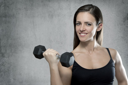 Beautiful sporty muscular woman with a dumbbell on gray background with place for textの写真素材