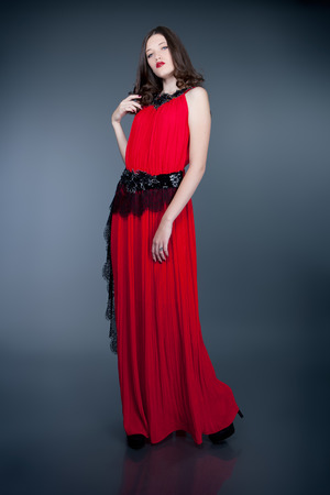 fashion model in red evening dress posing on gray backgroundの写真素材