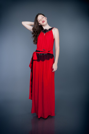fashion model in red evening dress posing on gray backgroundの写真素材