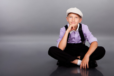 Old fashioned boy sitting and looking to the camera on gray backgroundの写真素材