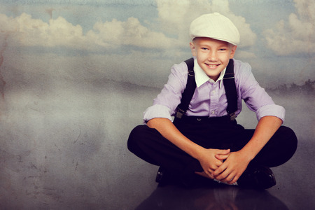 Old fashioned boy sitting and looking to the camera. Closeup. Photo in retro style with old textured paper.の写真素材