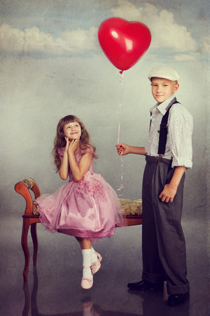 The boy gives a red balloon to the girl. Photo in retro style with old textured paper.の写真素材