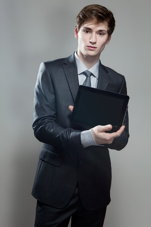 Portrait of young businessman showing touch screen computer, on gray backgroundの写真素材