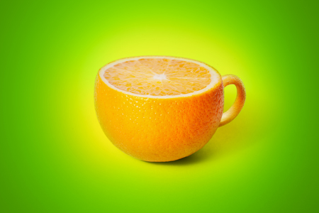 Cup of tea in the form of orange on green backgroundの写真素材