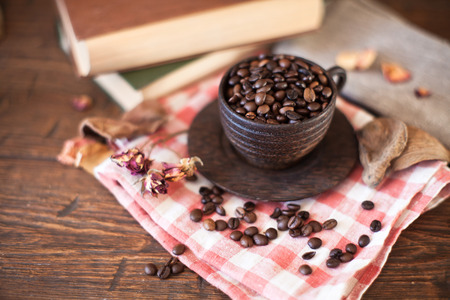 Wooden cup with coffee beans and books on old wooden tableの写真素材