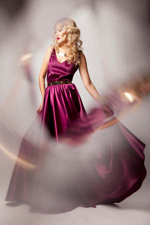 Beautiful woman model posing in elegant purple silk dress with frame of reflection in the studioの写真素材