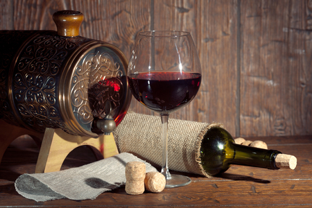 Wine bottle and small barrel with glass on old wooden background. Vintage colors.の写真素材