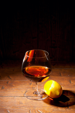 Glass of cognac with lemon on old wooden backgroundの写真素材