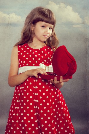 Little girl in vintage spotted red dress holding her present. Closeup. Photo in retro style with old textured paper.の写真素材