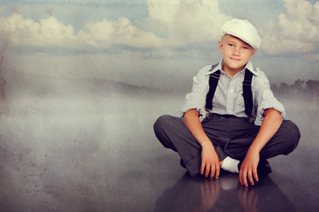Old fashioned boy sitting and looking to the camera. Closeup. Photo in retro style with old textured paper.の写真素材