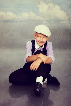 Old fashioned boy sitting and looking to the camera. Closeup. Photo in retro style with old textured paper.の写真素材