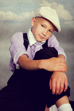 Old fashioned boy sitting and looking to the camera. Closeup. Photo in retro style with old textured paper.の写真素材