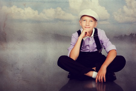 Old fashioned boy sitting and looking up. Closeup. Photo in retro style with old textured paper.の写真素材