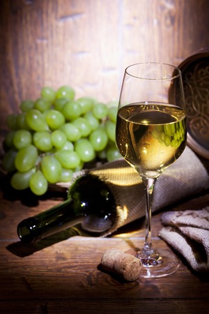 Wine bottles, small barrel,  bunch of grapes and with glass of white wine on old wooden backgroundの写真素材