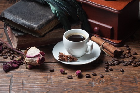 Cup of coffee, dry rose, old books, crow quills and coffee grinder on wooden table. Vintage still life.の写真素材