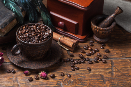 Cup of coffee, dry rose, old books, crow quills and coffee grinder on wooden table. Vintage still life.の写真素材