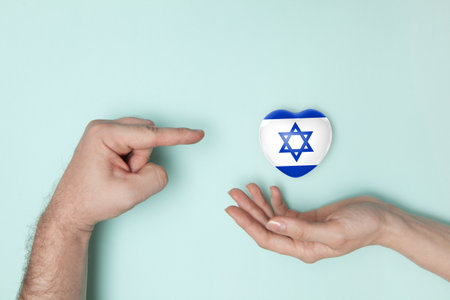 Woman hands holding heart with print of Israel flag and man hand pointing to the heart. Flat lay. Copy space.の写真素材