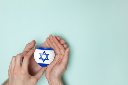 Heart with print of Israel flag in female and male hands. Flat lay. Copy space.の写真素材