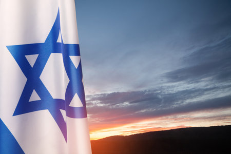 Israel flag with a star of David over cloudy sky background on sunset. Patriotic concept about Israel with national state symbols. Banner with place for text.の写真素材