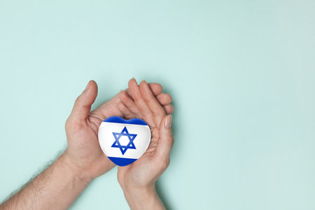 Heart with print of Israel flag in female and male hands. Flat lay. Copy space.の写真素材
