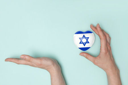 Female hands with small heart with print of Israel flag and palm for your offers. Flat lay. Copy space.の写真素材
